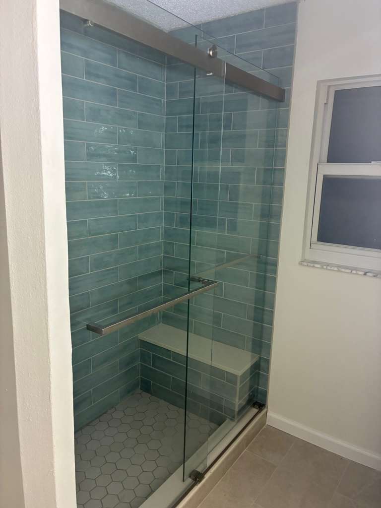 Shower remodel with turquoise brick tile glass door and built-in bench in North Port FL