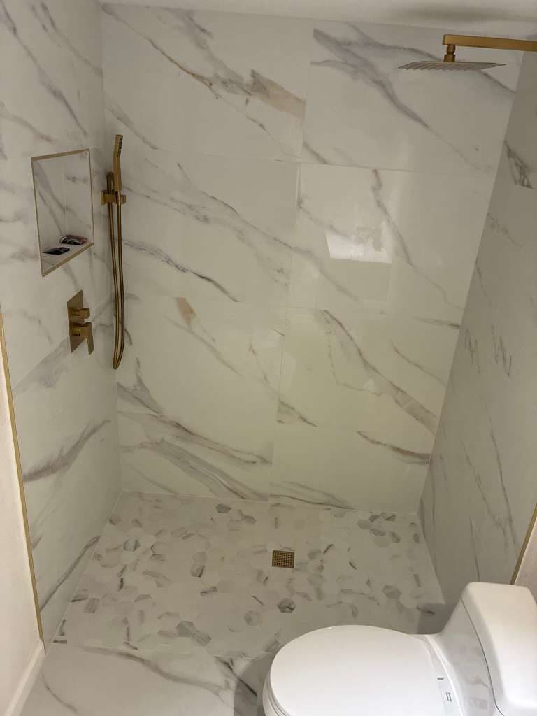 Walk-in shower with marble tile gold fixtures and hexagon floor in North Port FL