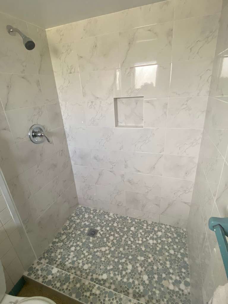 Walk-in shower with white marble tile and pebble floor in North Port FL
