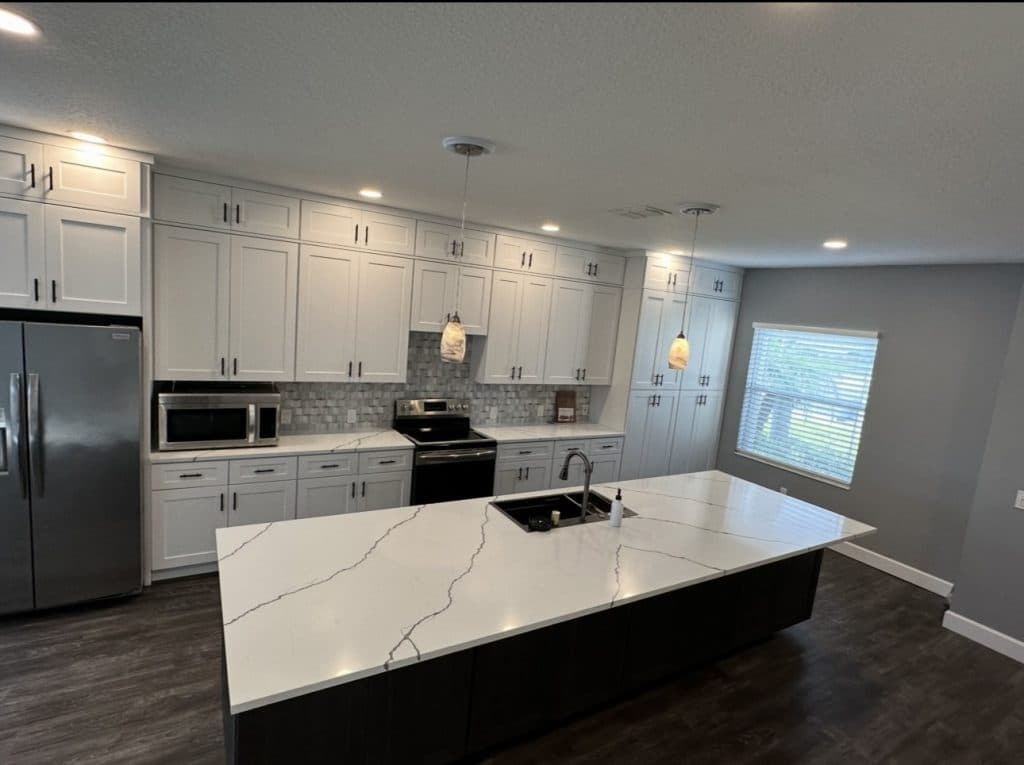Full kitchen renovation with white cabinets quartz countertops and pendant lighting